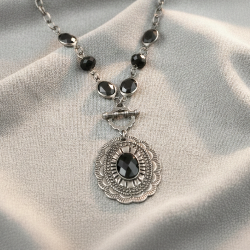 Silver necklace with black beads and a decorative pendant on a light gray fabric background