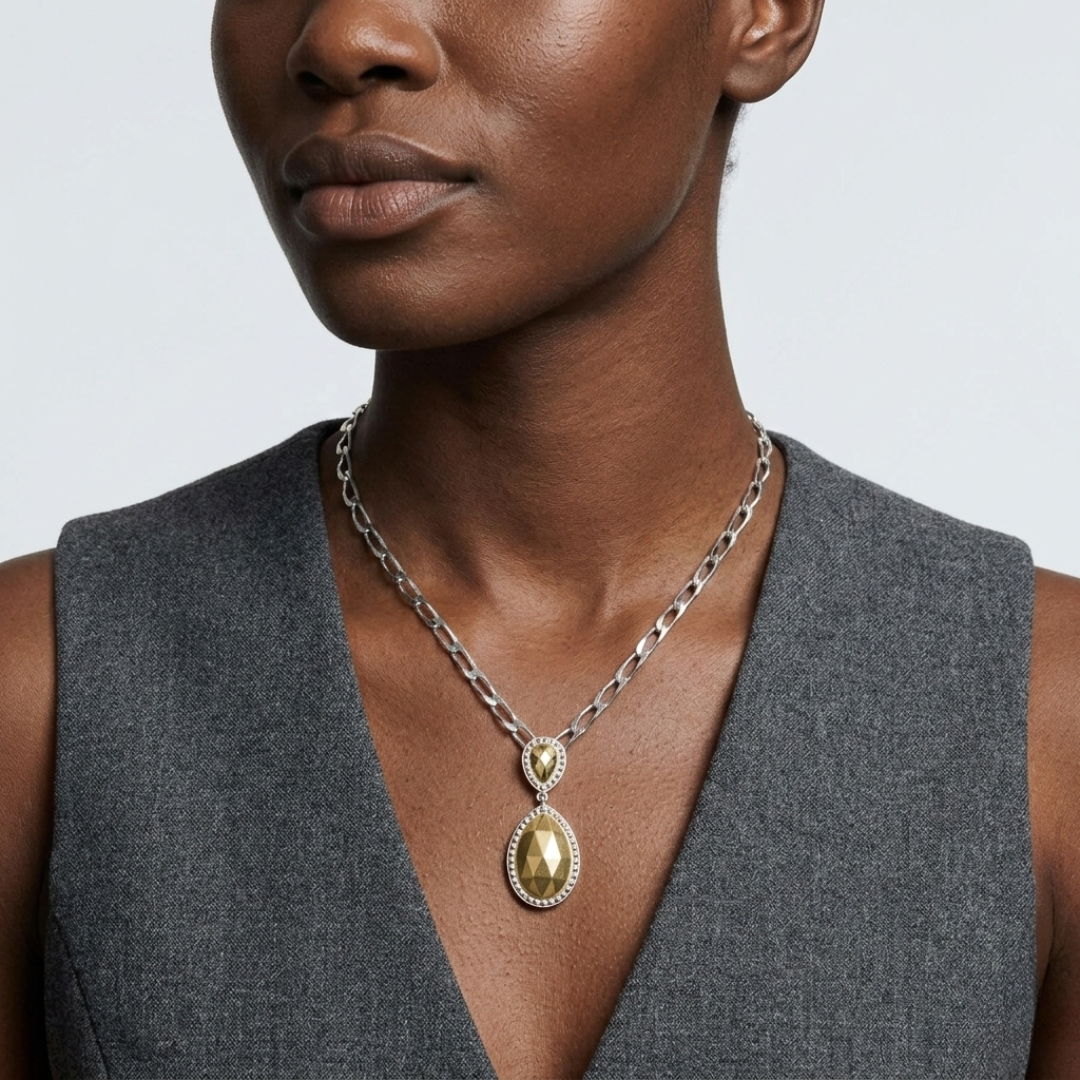 Woman wearing a shiny silver tone necklace with a fusion lux teardrop pendant on gray top against a light background