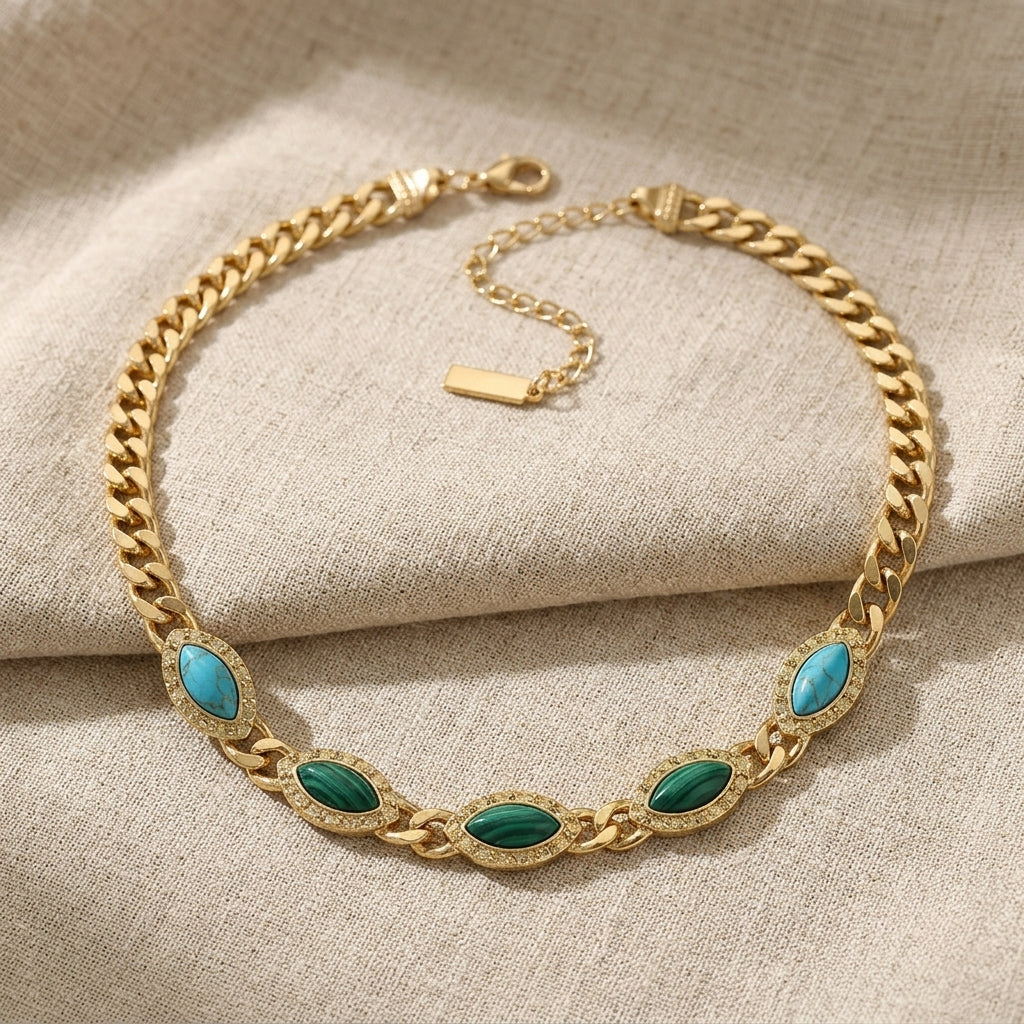 Gold chain bracelet with green and turquoise stones on a beige fabric background
