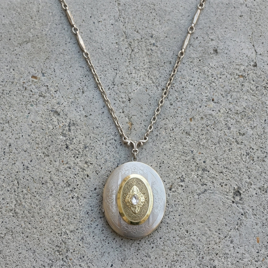 Necklace with an oval locket pendant featuring a gold design on a concrete surface
