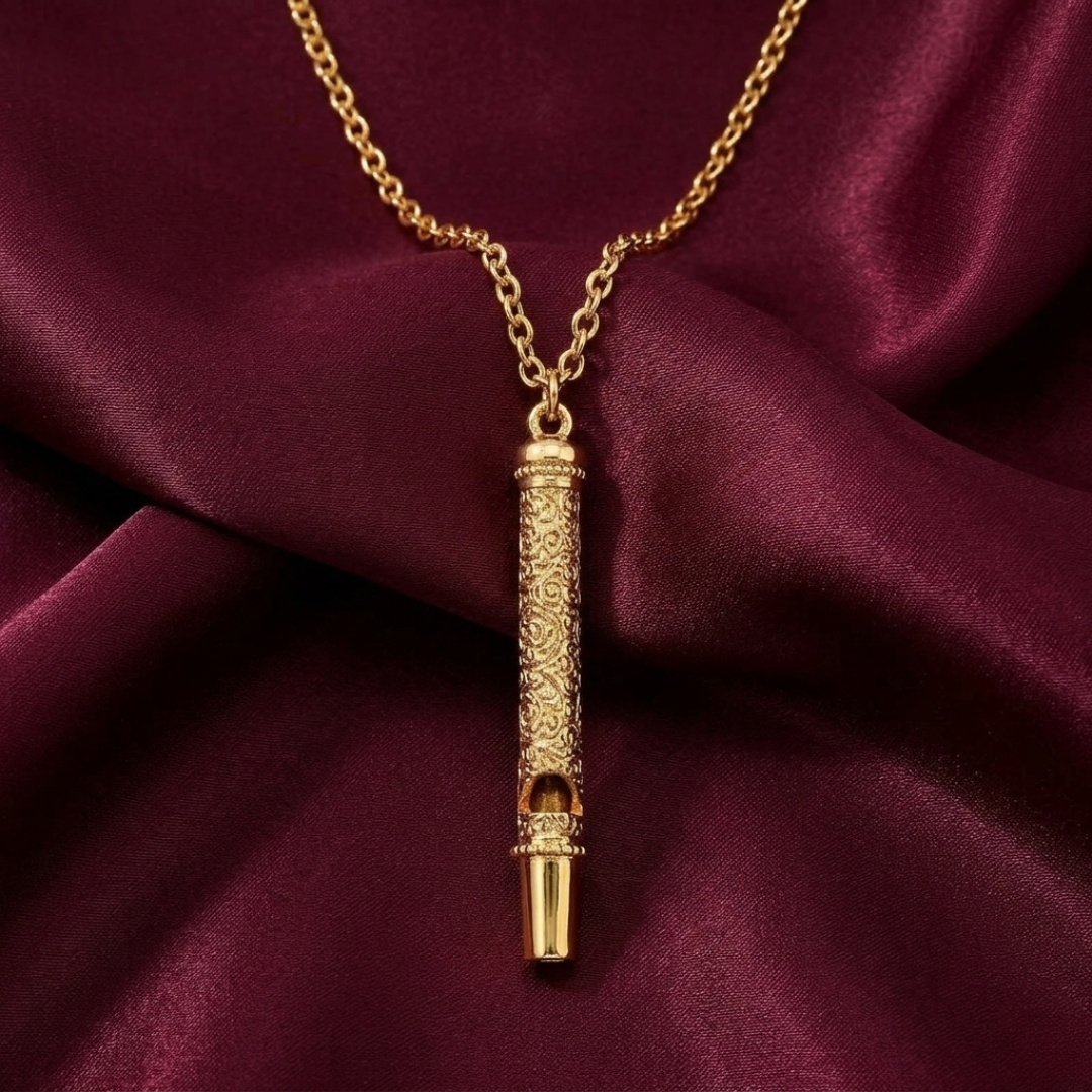 Gold necklace with a decorative whistle pendant on a burgundy fabric background