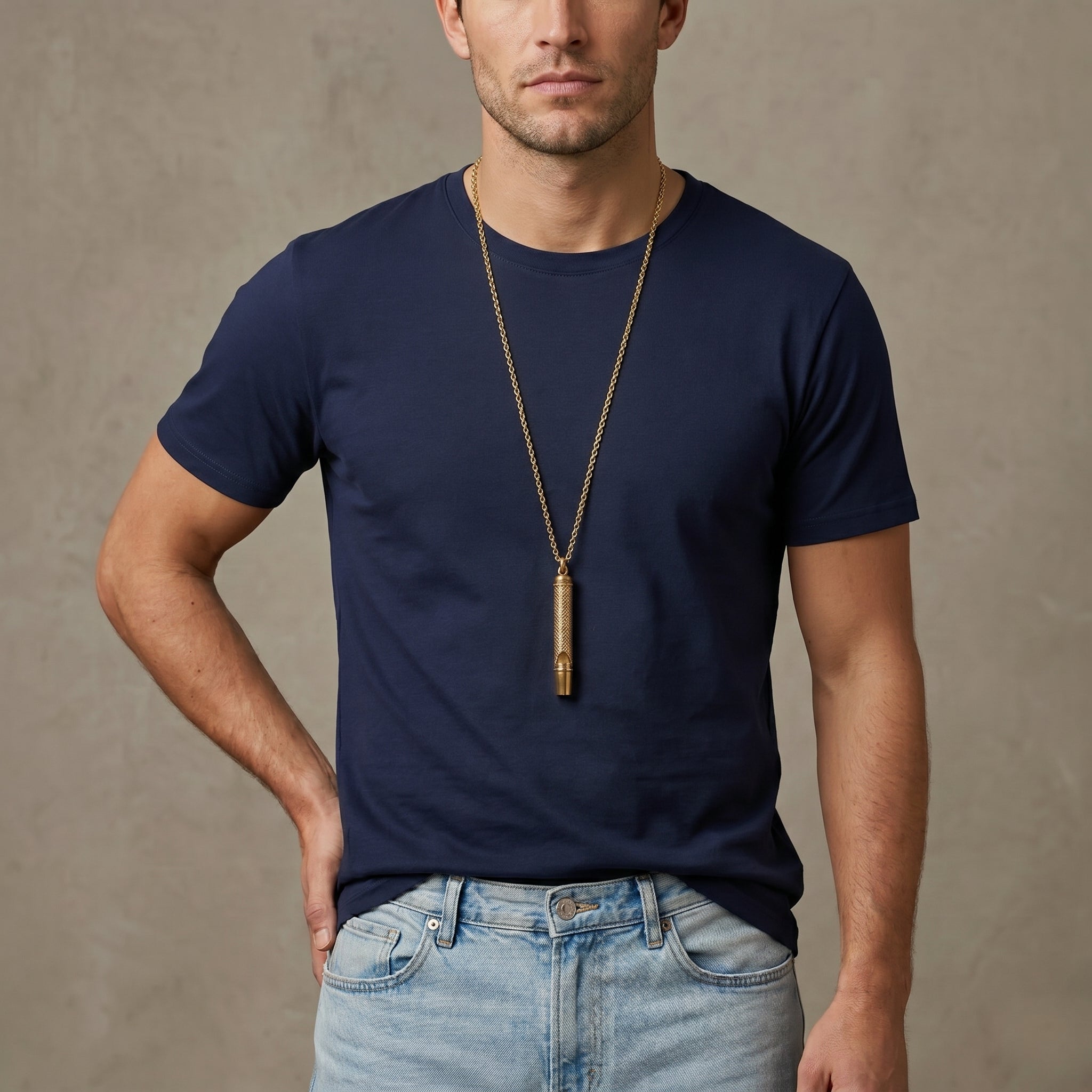 Man wearing a navy blue t-shirt and light blue jeans with a gold whistle pendant necklace against a beige background