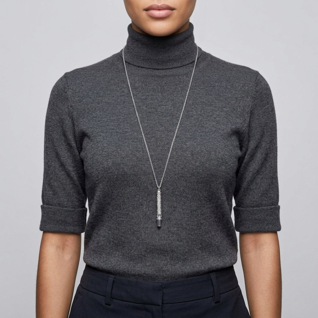 Person wearing a dark gray turtleneck sweater with a whistle necklace on a light gray background