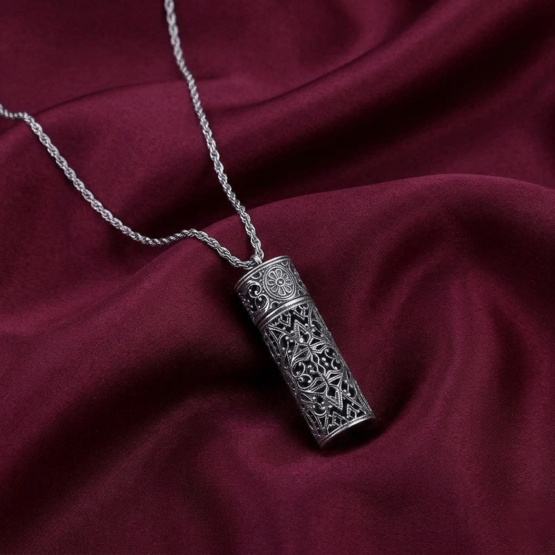 Silver necklace with an intricate vial pendant on a maroon fabric background