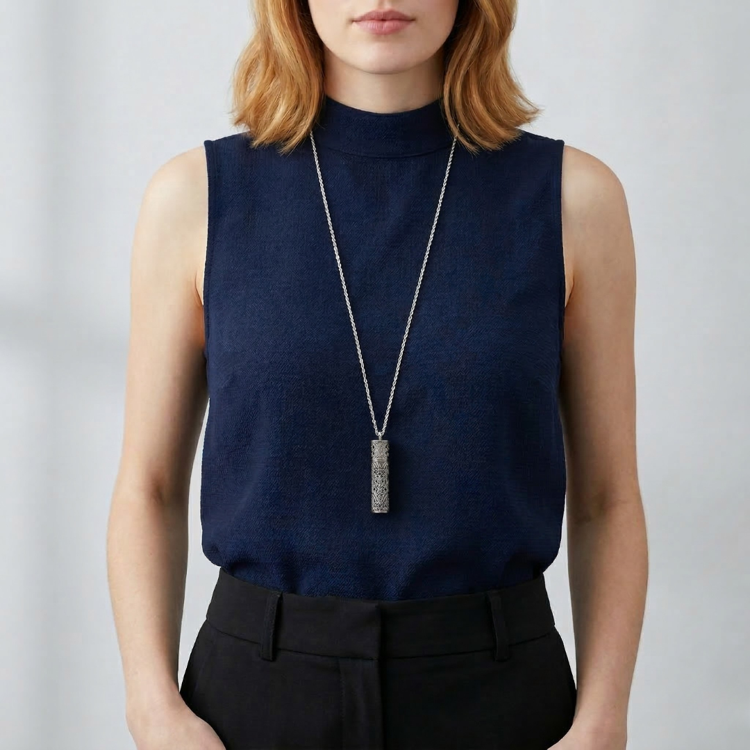Person wearing a navy sleeveless top with a long vial pendant necklace against a plain background