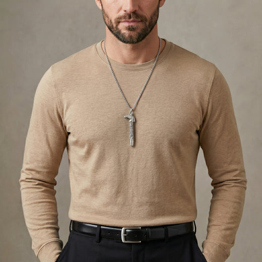 Man wearing a beige long-sleeve shirt with a horse whistle pendant necklace against a neutral background