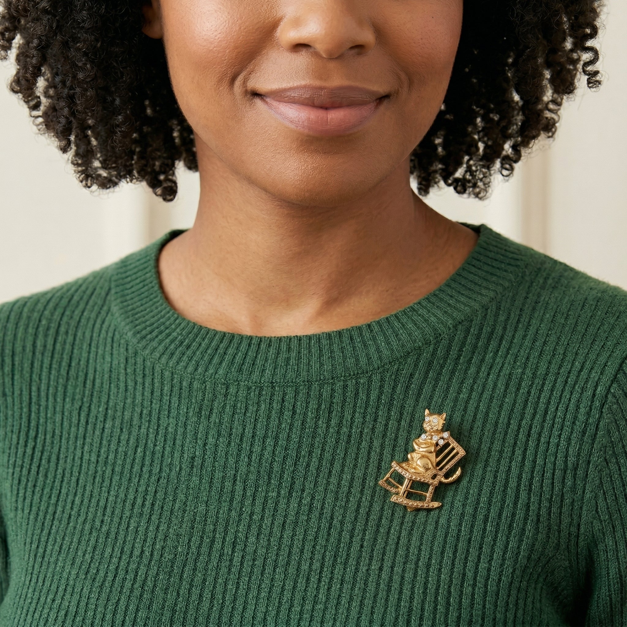 Woman wearing a green sweater with a cat on a rocking chair brooch, against a neutral background