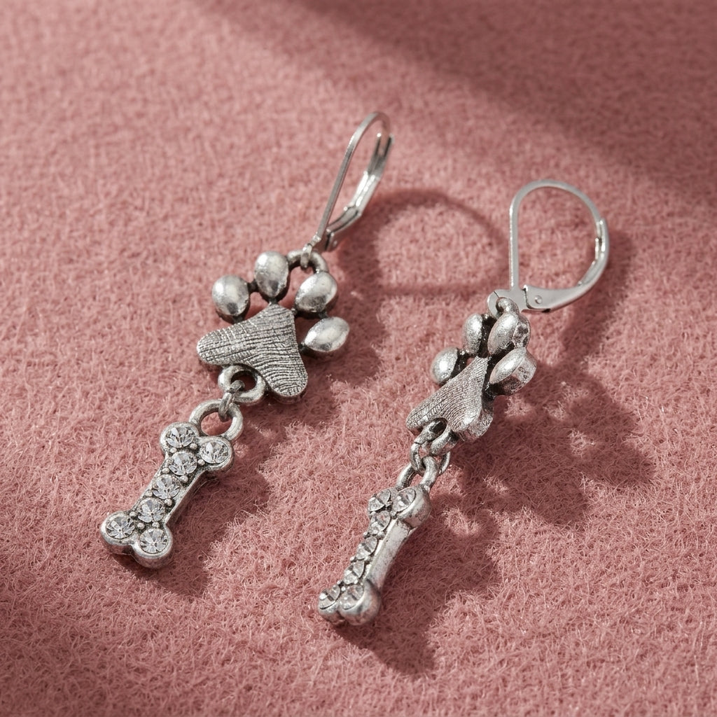 Paw & Clear Crystal Bone Dangling Earrings resting on pink felt