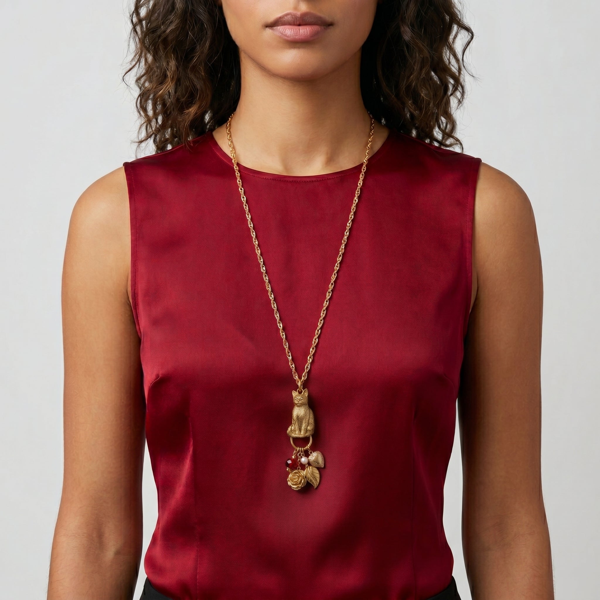 Person wearing a red top and a gold tone necklace with a cat pendant and several dangling charms