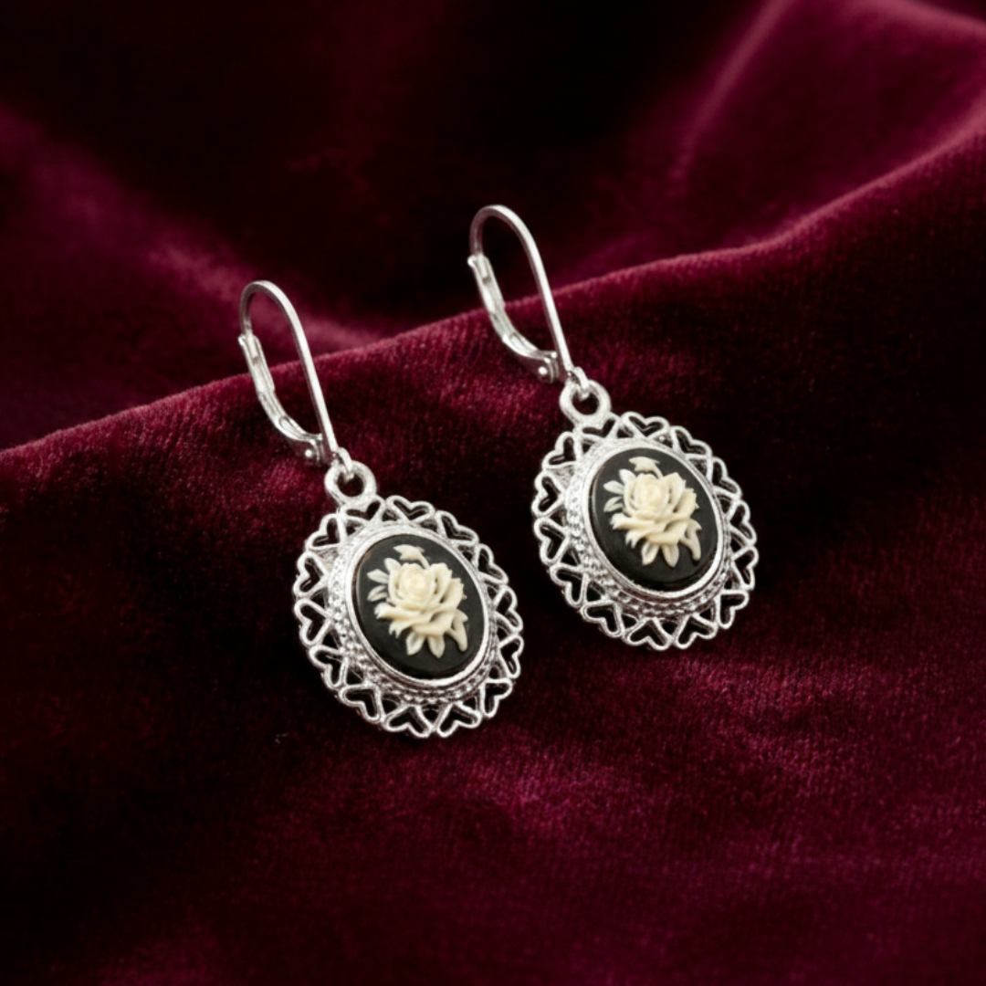 Pair of silver earrings with floral designs on a dark red fabric background