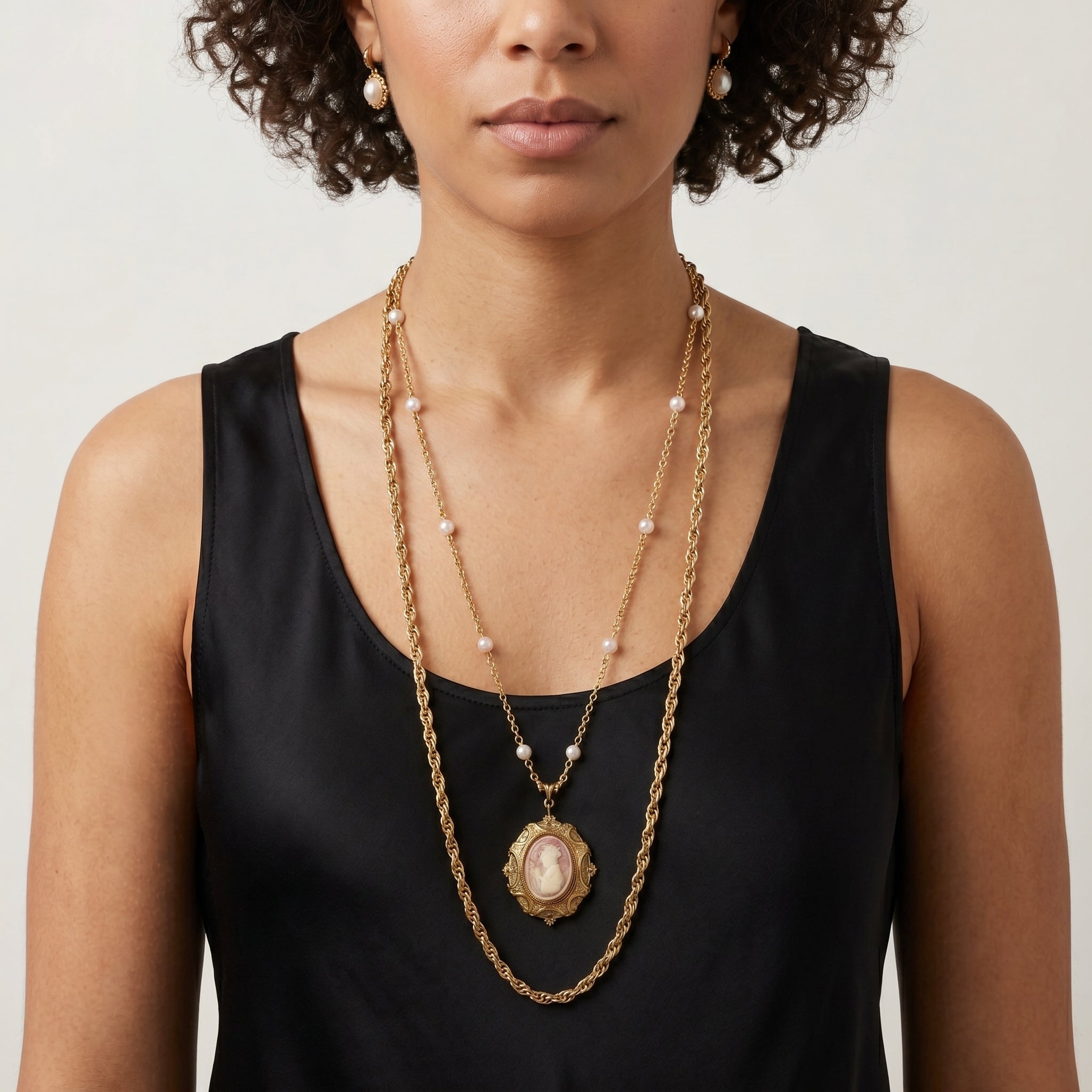 Woman in a black top wearing two necklaces, one with faux pearl accents on a gold tone chain and a red and ivory cameo pendant, the other a plain gold tone chain necklace.