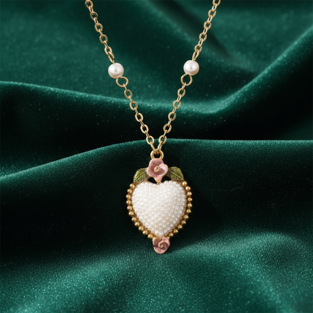 Necklace with a heart-shaped pendant filled with small, decorative faux pearls and light pink roses on a green fabric background