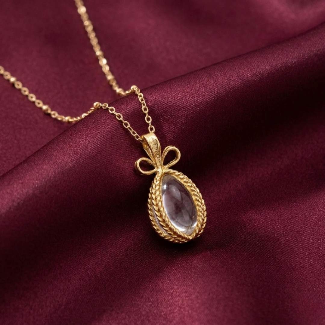 Gold necklace with a clear glass egg-shaped pendant on a maroon fabric background