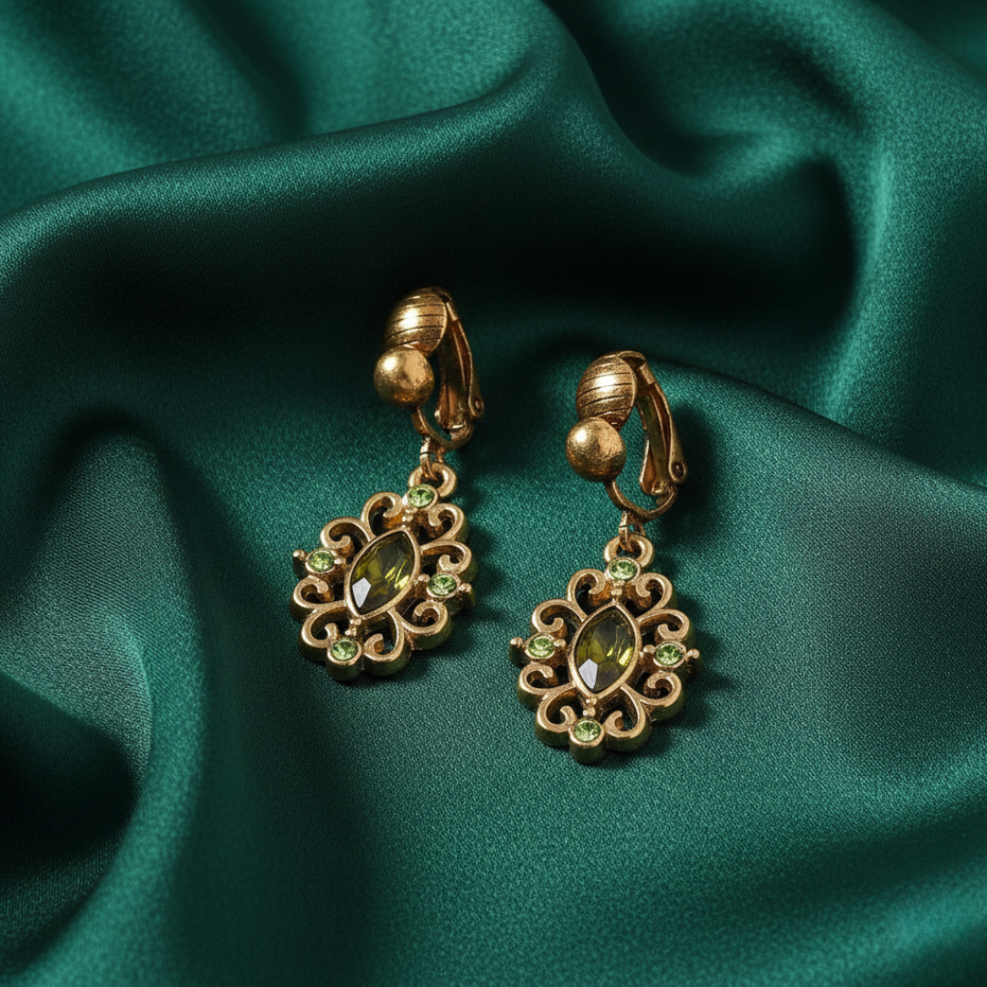 Gold earrings with green gemstones on a green fabric background