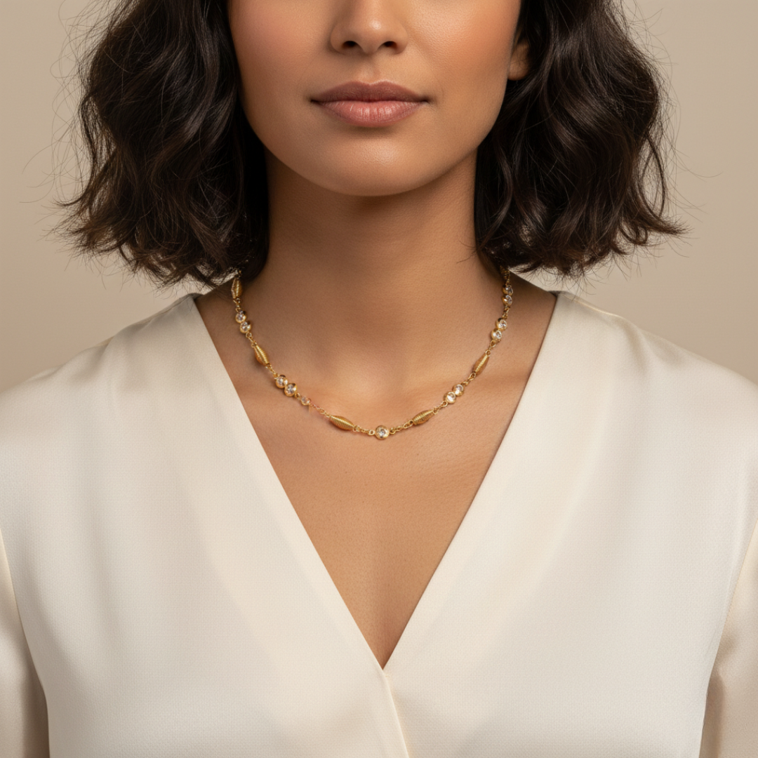 Woman wearing a gold necklace with clear crystals against a neutral background