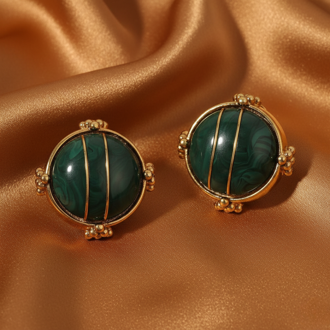 Pair of gold and green earrings on a brown satin background