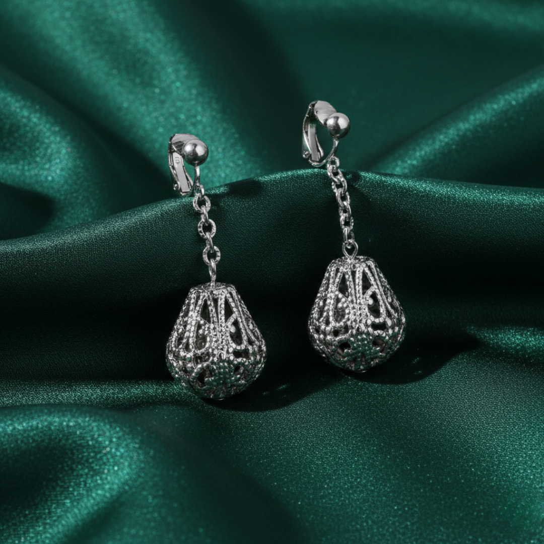 Silver earrings with intricate designs on a green satin background