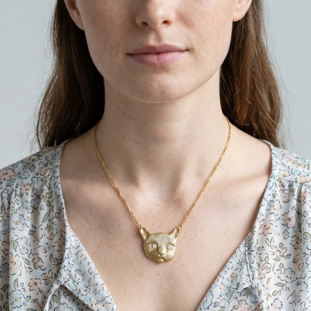 Woman wearing a gold cat-shaped pendant necklace against a neutral background