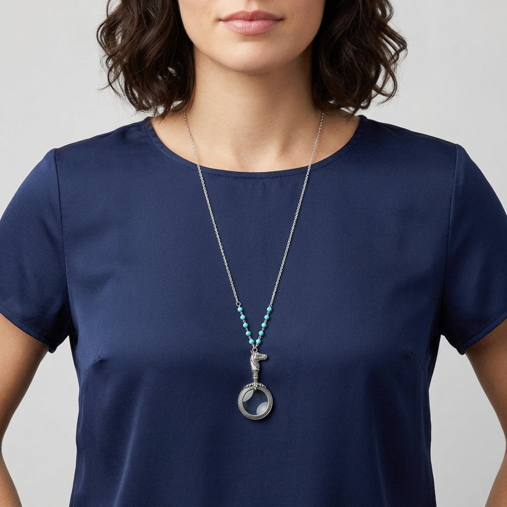Woman wearing a blue shirt and a necklace with a magnifying glass equestrian pendant on a plain background