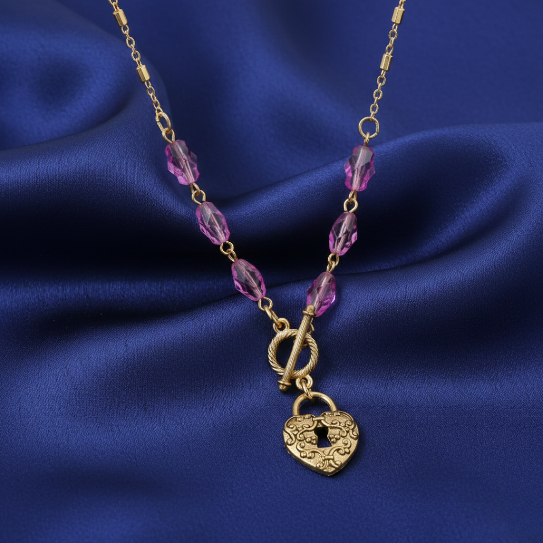 Gold necklace with purple beads and a heart-shaped lock pendant on a blue fabric background