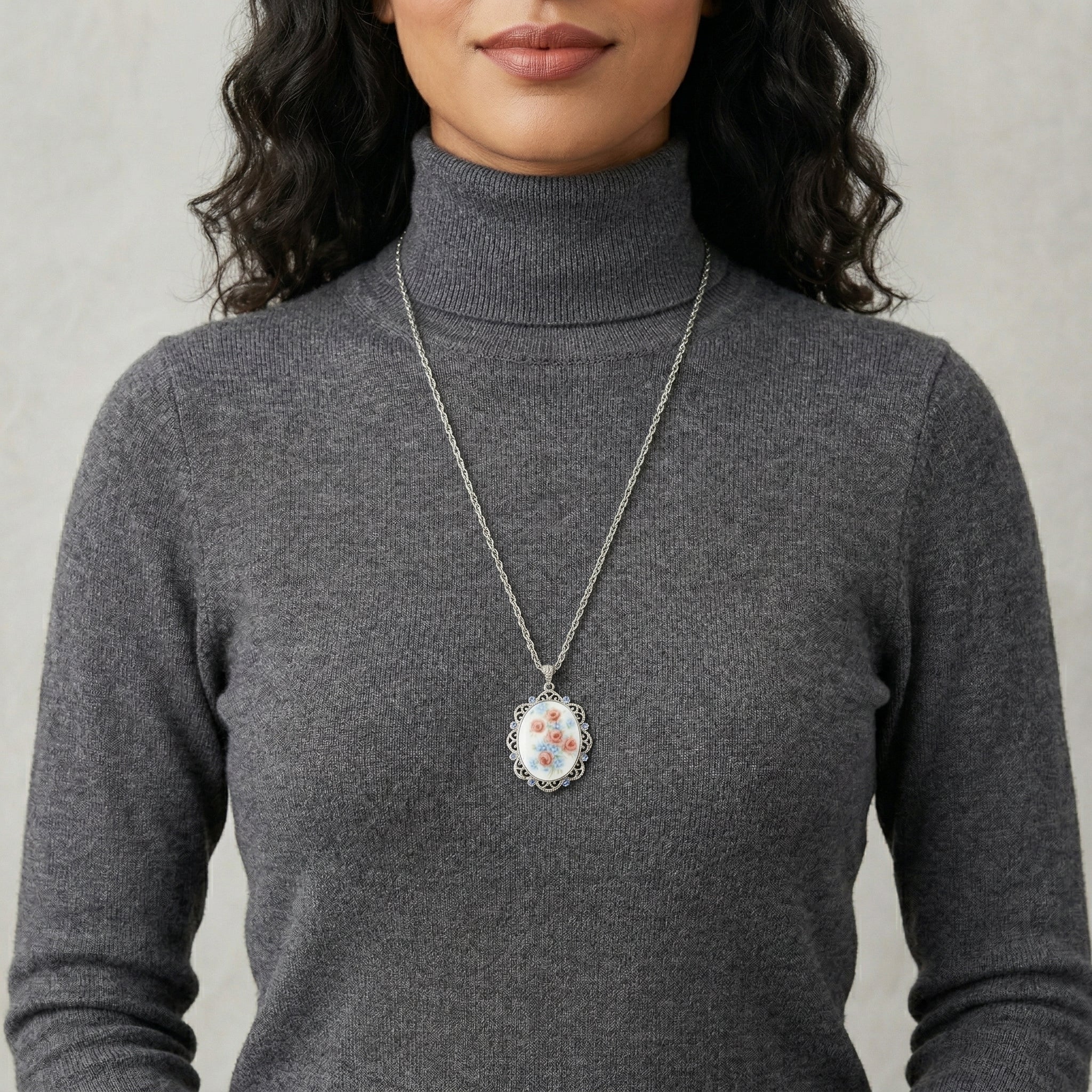 Person wearing a gray turtleneck sweater with a long necklace featuring a floral pendant.