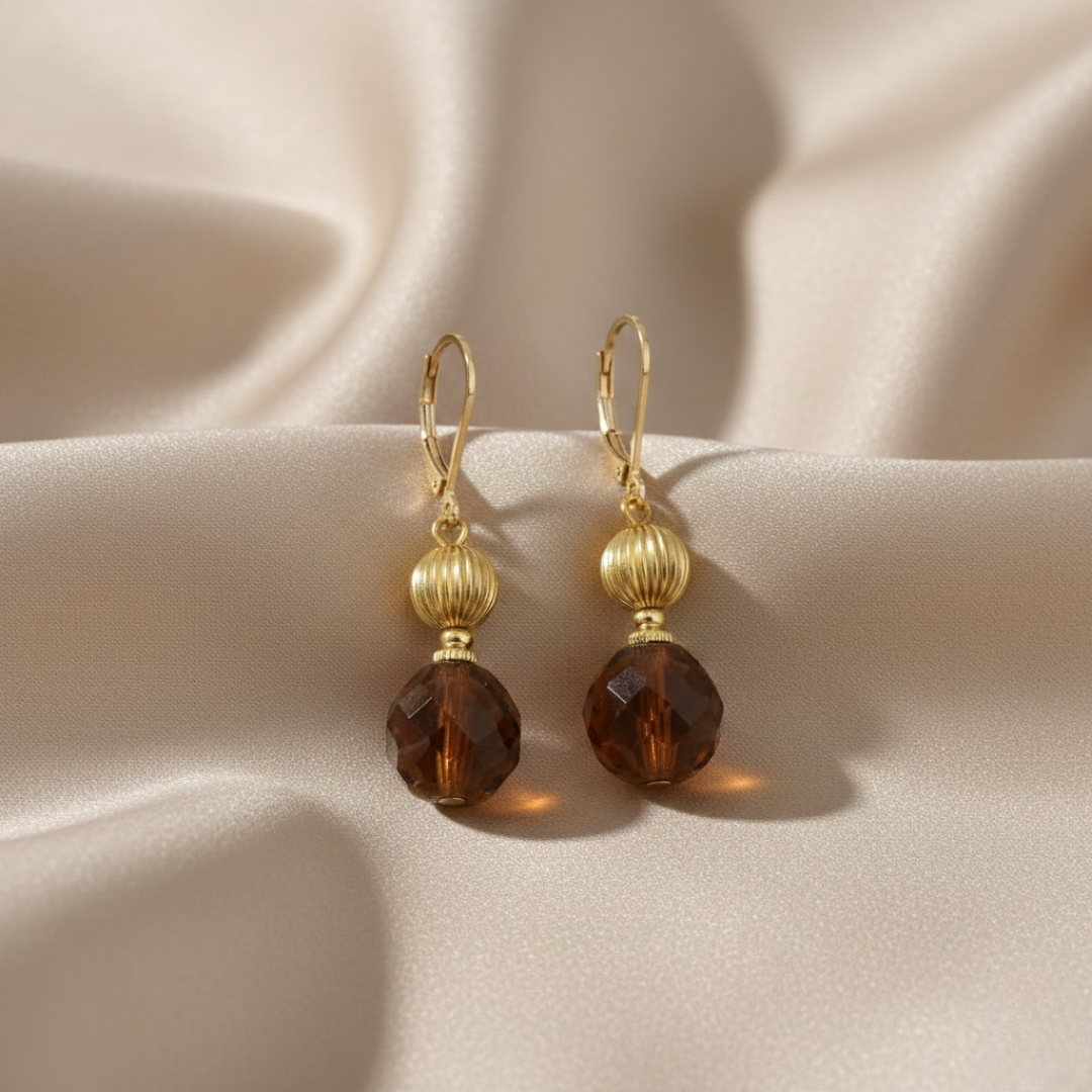 Gold earrings with brown crystals on a beige fabric background
