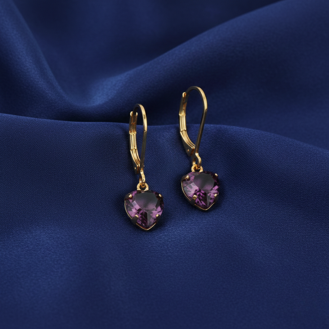 Gold heart-shaped earrings with purple crystals on a blue fabric background