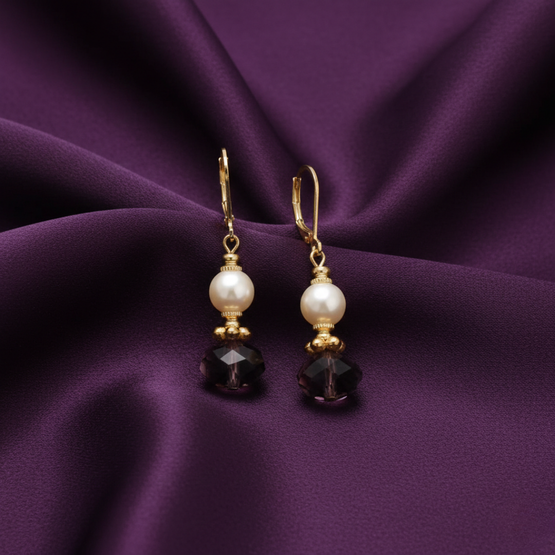 Pair of earrings with faux pearls and purple crystals on a purple fabric background