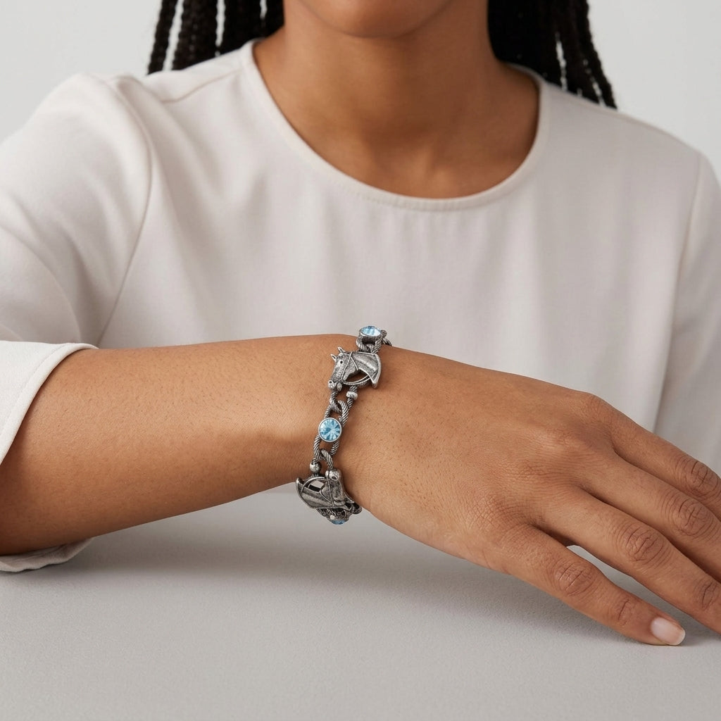 Person wearing a silver bracelet with horse head design and blue crystals on a plain background