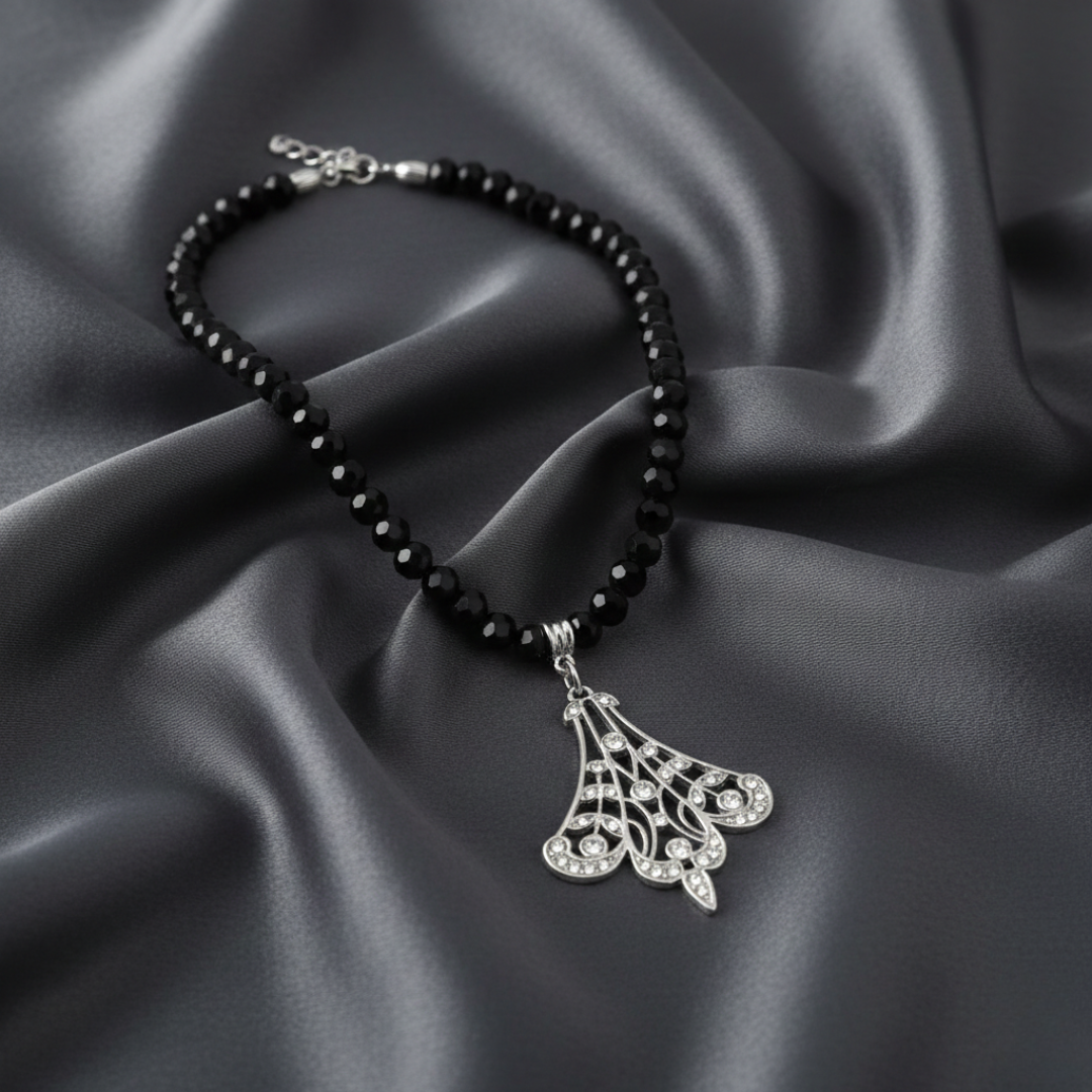 Black beaded bracelet with a silver filigree pendant on a dark fabric background