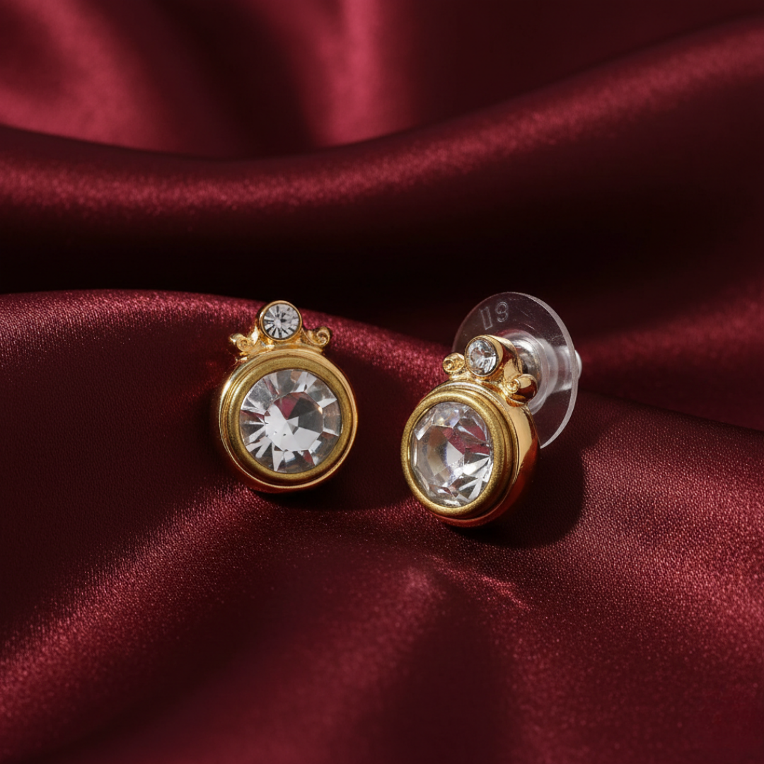 Gold earrings with clear gemstones on a red satin background