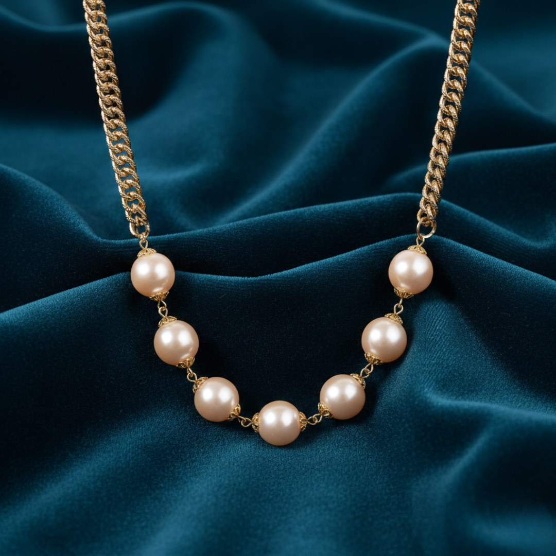 Champaign-colored faux pearl necklace with gold chain on a blue fabric background
