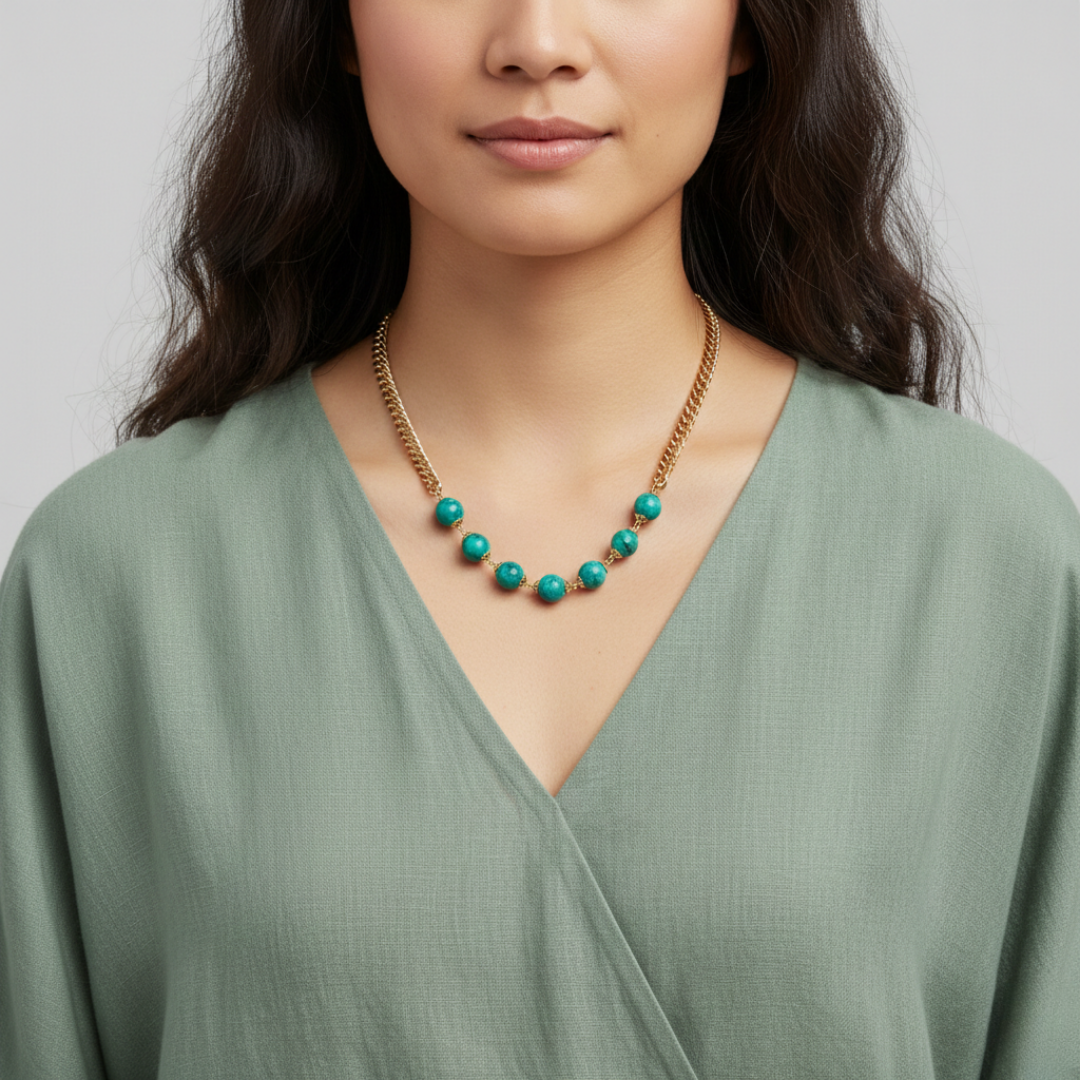 Woman wearing a green dress and gold necklace with turquoise beads against a gray background