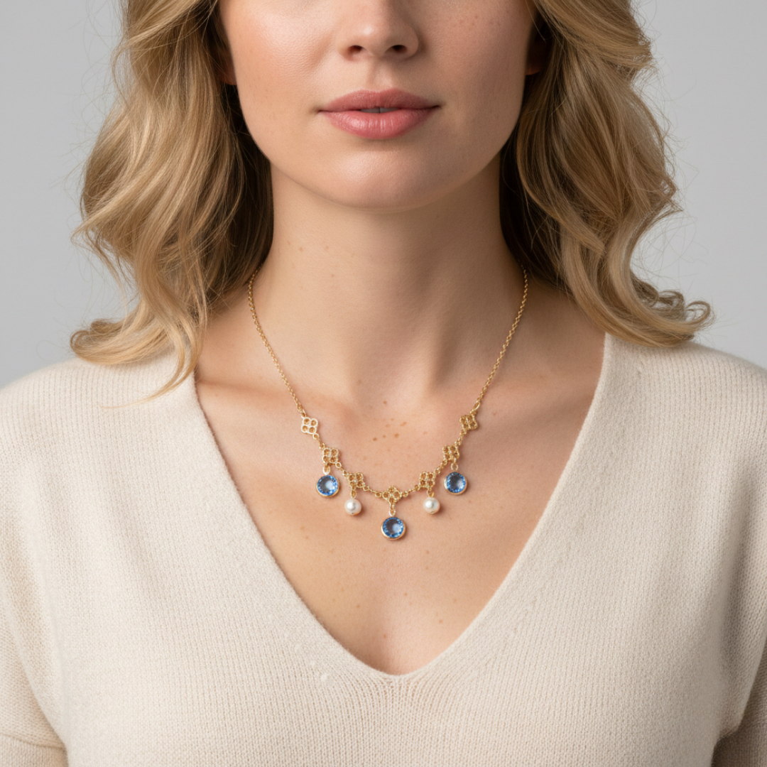 Woman wearing a gold necklace with blue gemstones and faux pearls on a neutral background