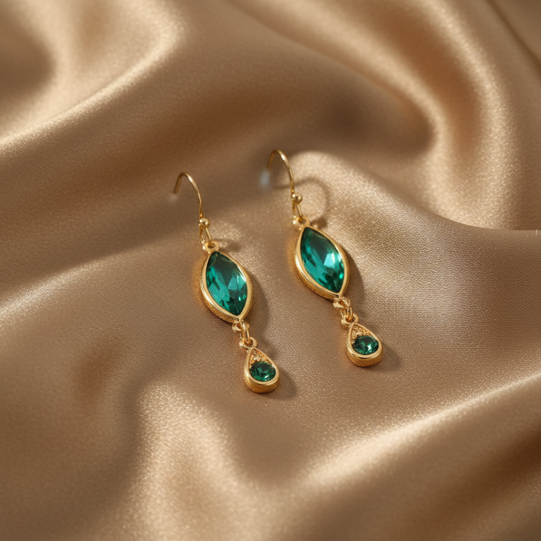 Gold earrings with green crystals on a beige satin background