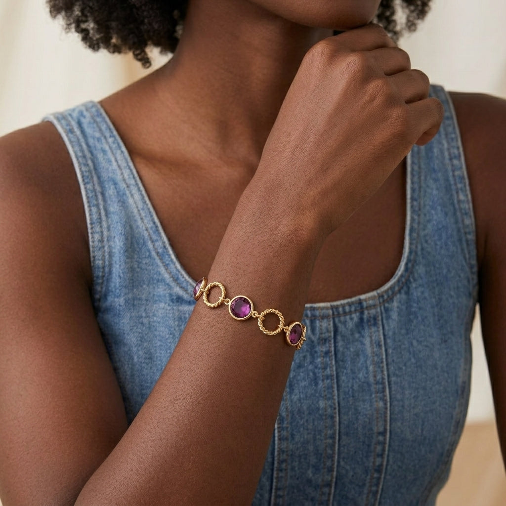Woman wearing a gold bracelet with purple Austrian crystals on a neutral background