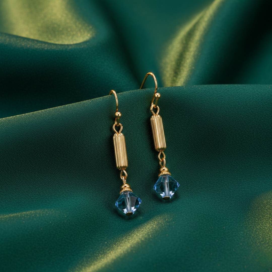 Gold earrings with blue crystals on a green fabric background