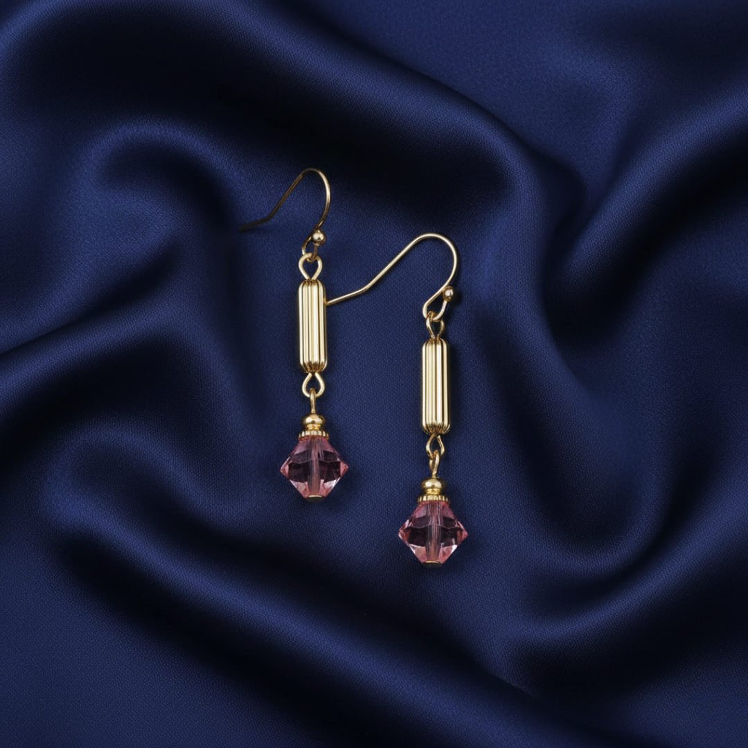 Gold earrings with pink crystals on a blue satin background