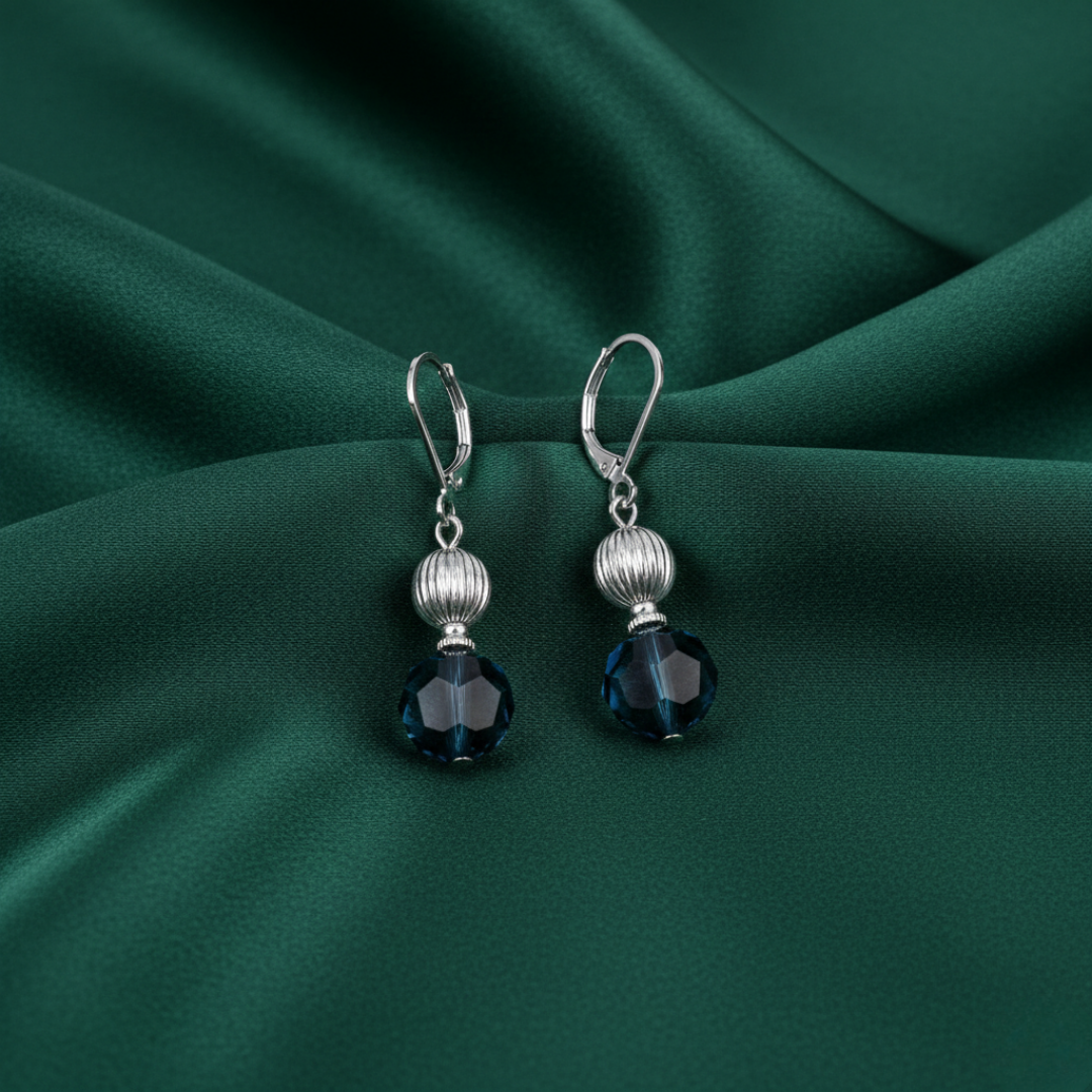 Silver earrings with blue crystals on a green fabric background