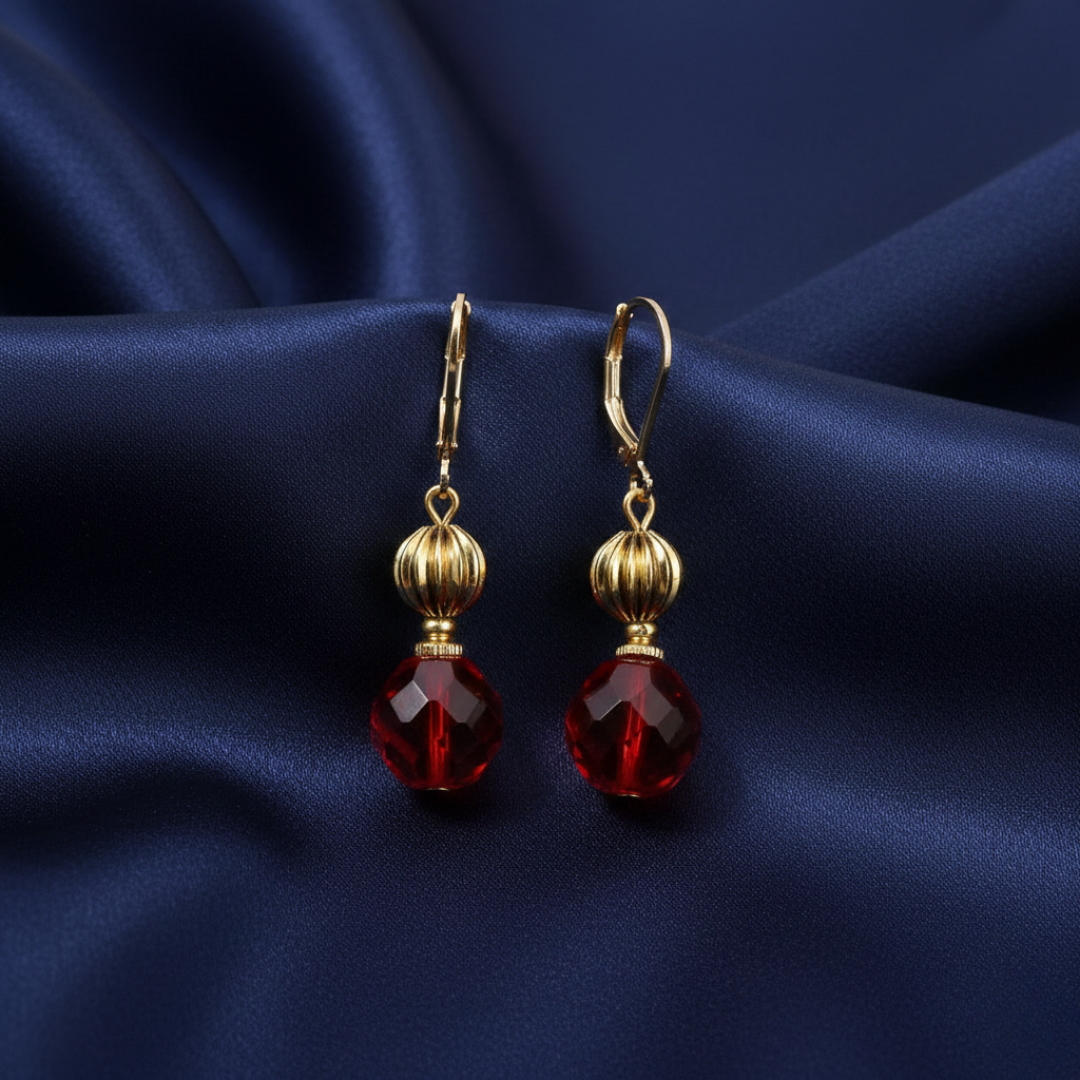 Gold earrings with red crystals on a blue satin background