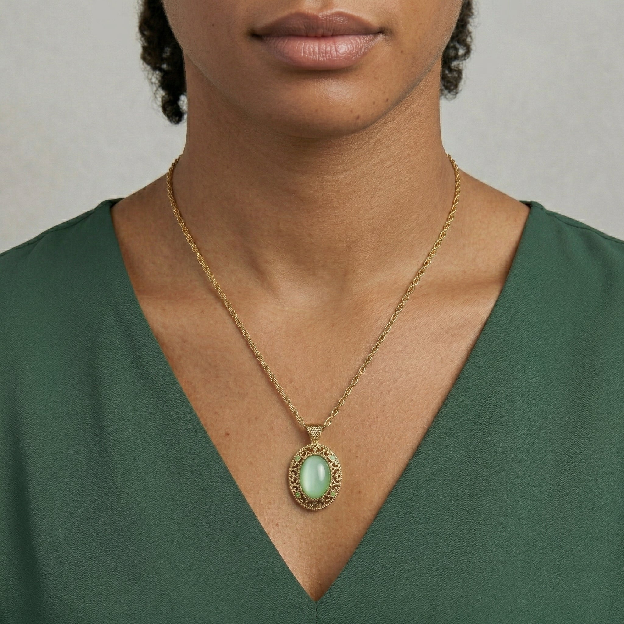 Woman wearing a gold necklace with a green pendant against a neutral background