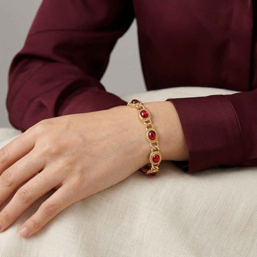 Gold bracelet with red stones on a wrist against a neutral background