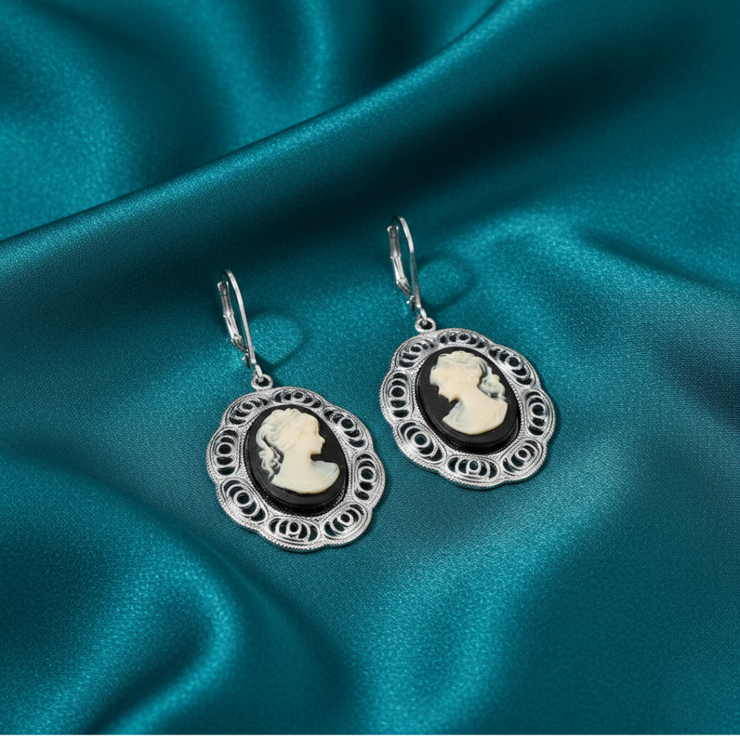 Silver earrings with black cameo design on a teal satin background