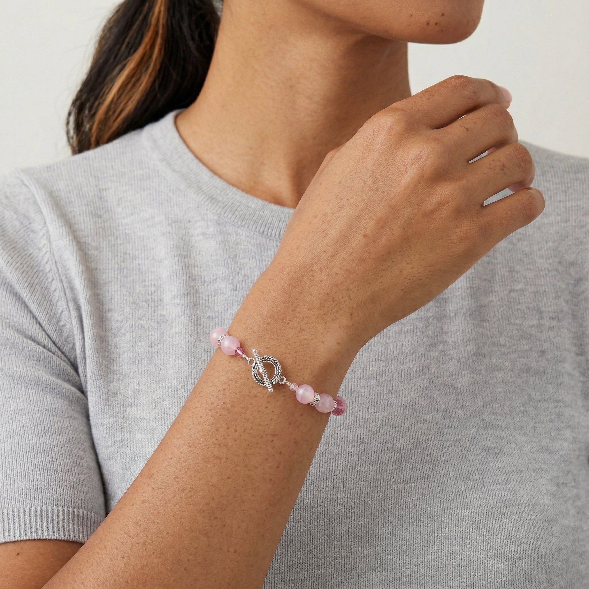 Person wearing a pink beaded bracelet with a silver charm on a plain background
