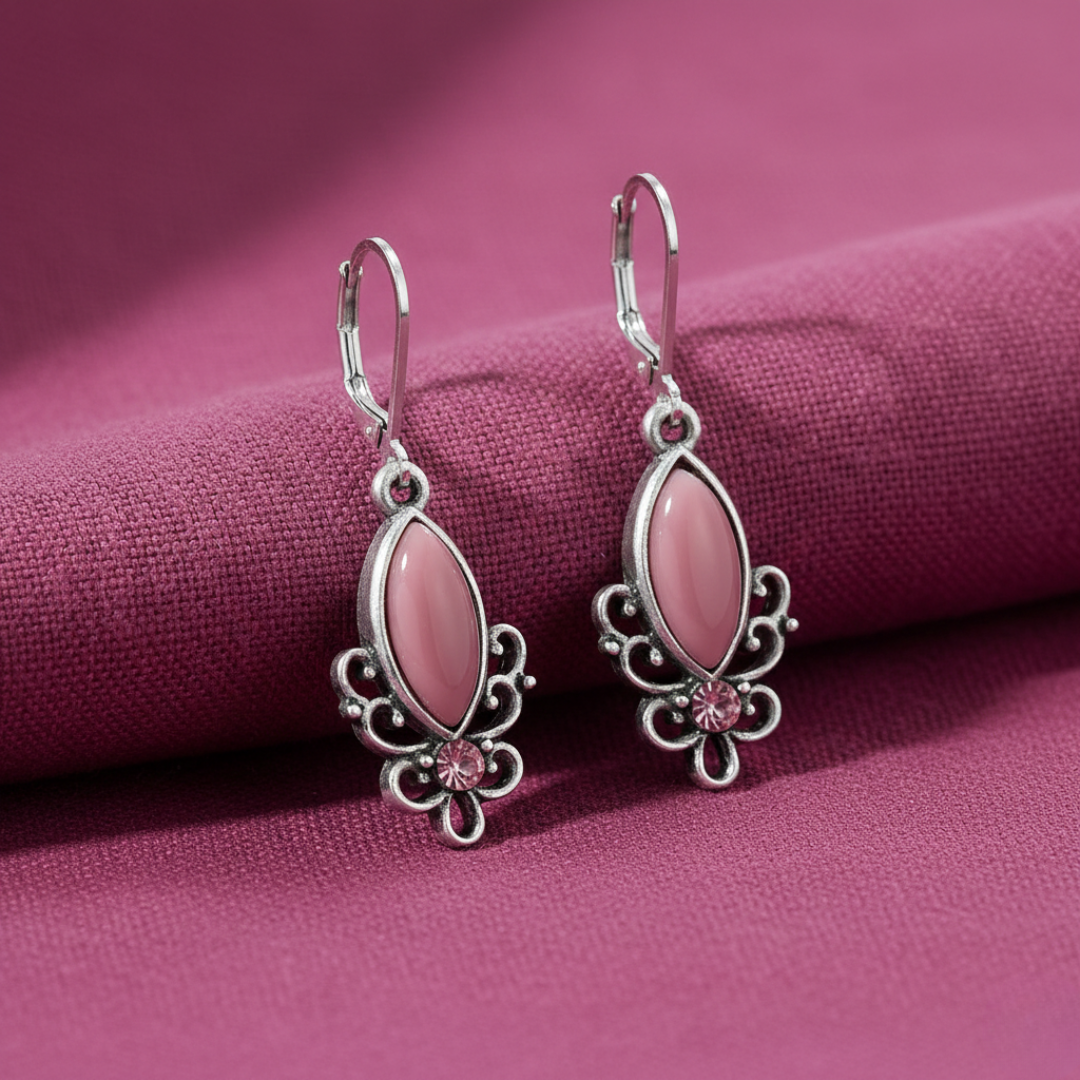 Pink moonstone earrings with silver accents and a pink crystal against a pink fabric background