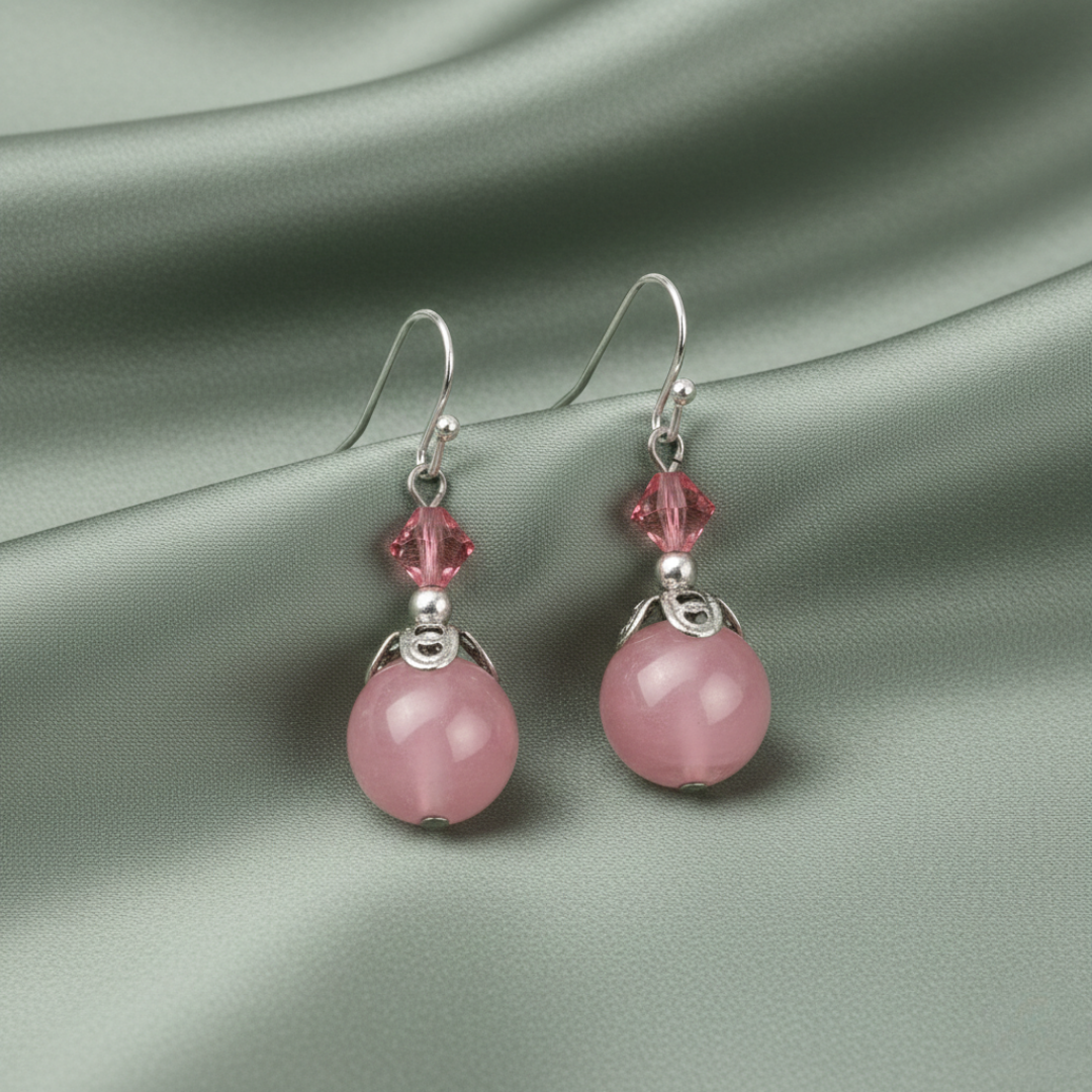 Pink crystak earrings with silver hooks on a gray fabric background
