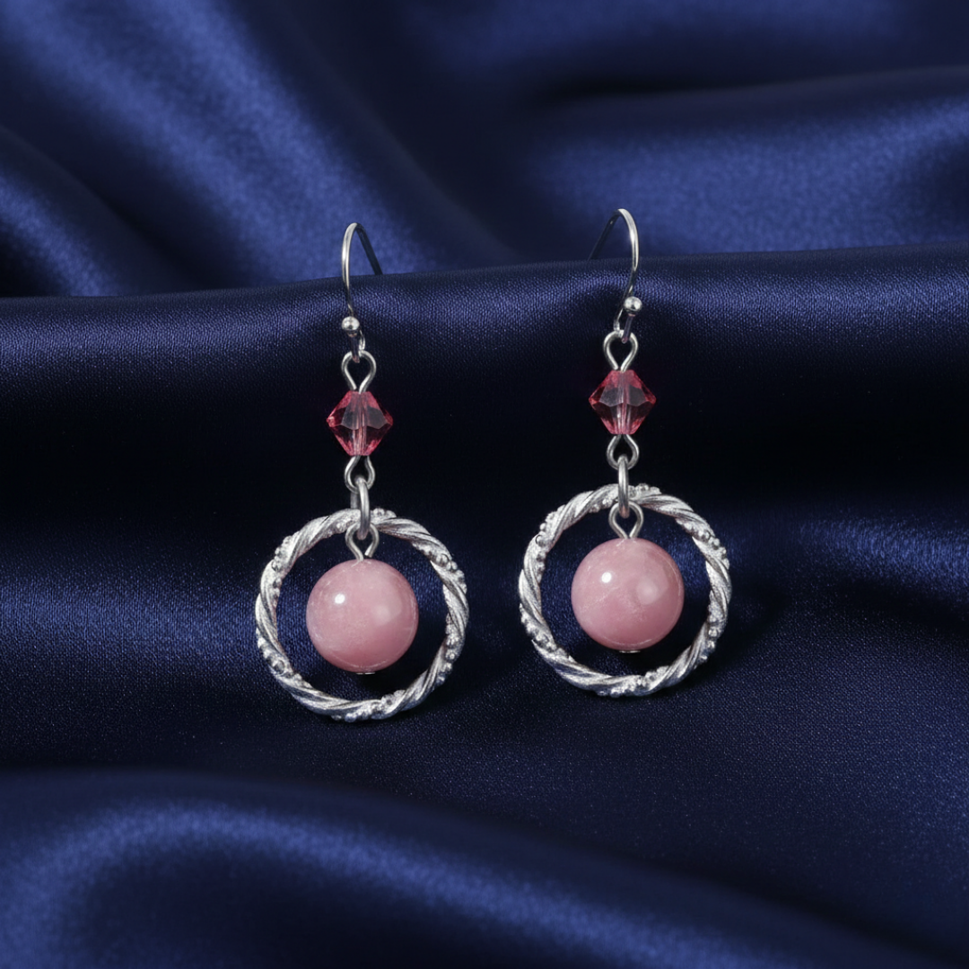 Pair of earrings with pink gemstones and pink crystals on a blue fabric background