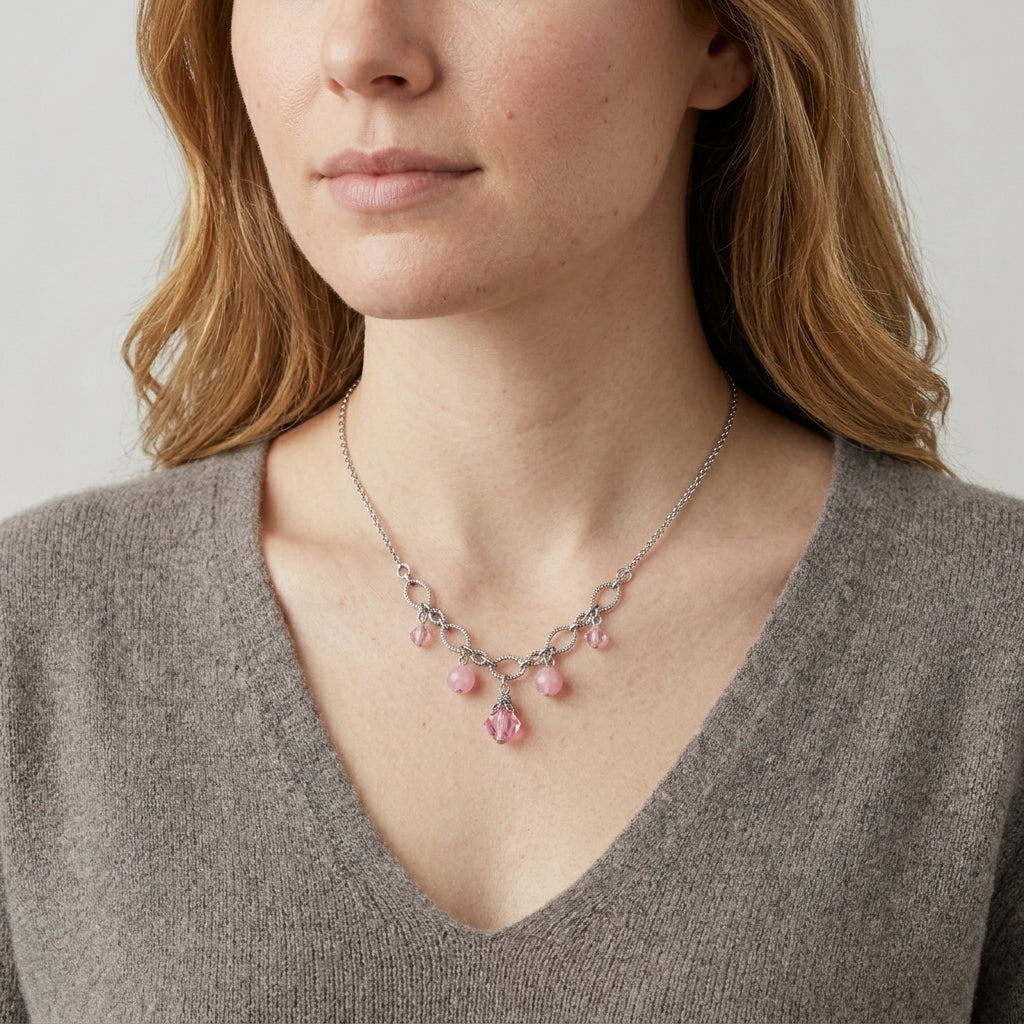 Woman wearing a delicate necklace with pink stones and crystals against a neutral background