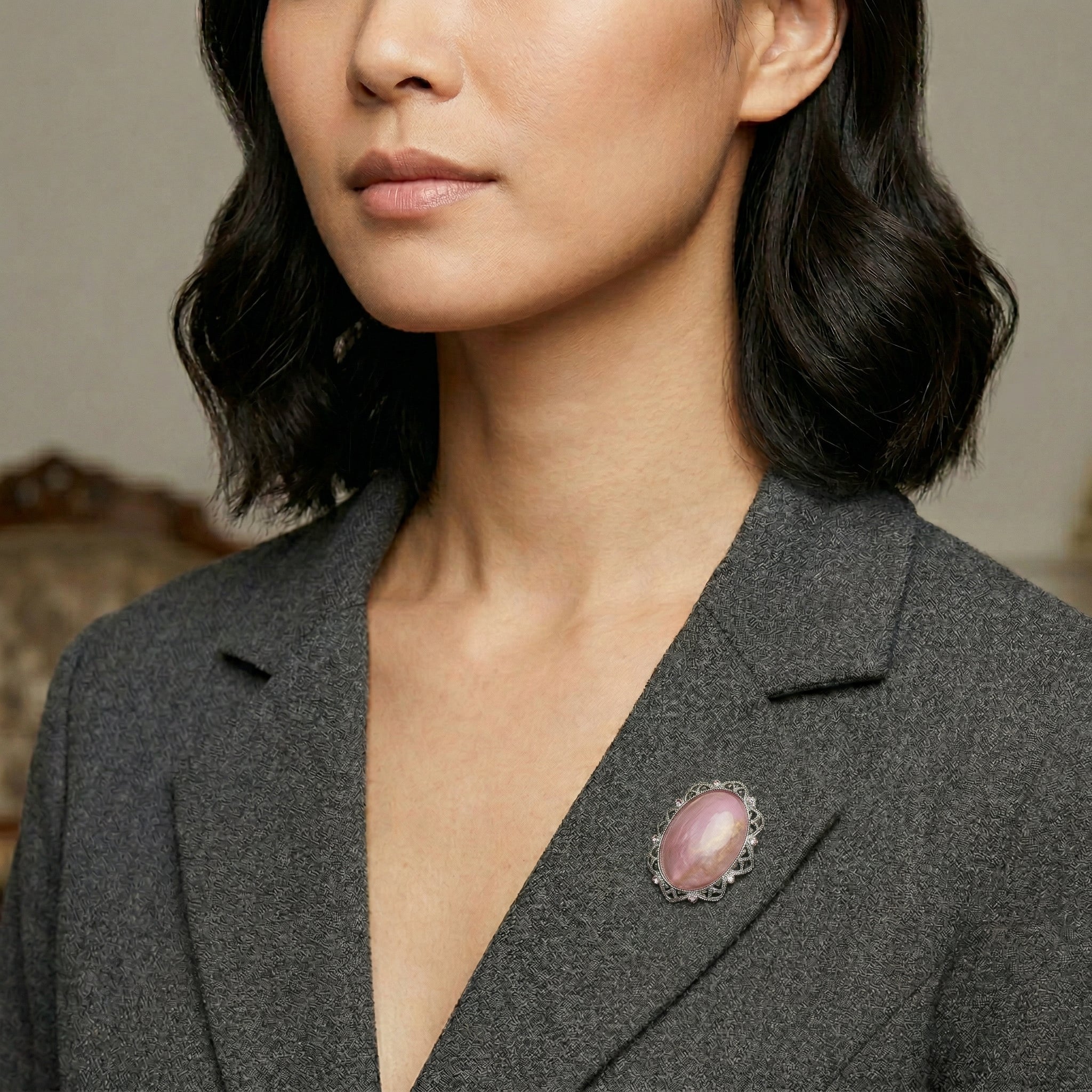 Woman wearing a gray blazer with a pink brooch against a neutral background