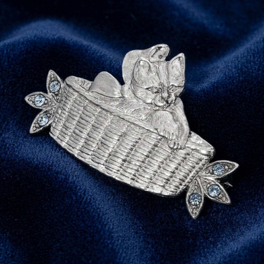 Silver brooch of a kitten in a basket on a blue fabric background